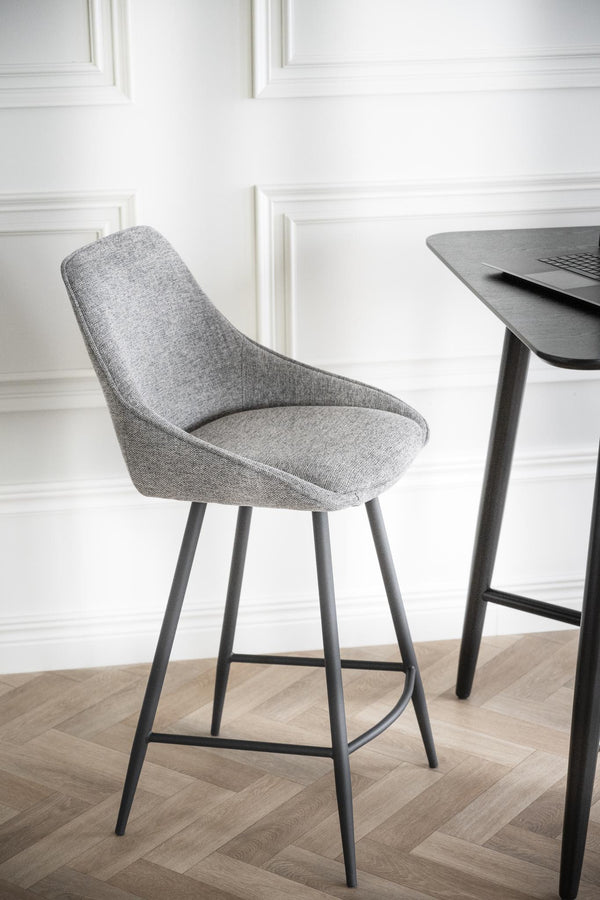 Grå stoppad barstol med metallben vid svart barbord mot vit panelvägg