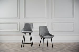 Grå stoppad matstol och barstol med svarta ben framför vit vägg med panel