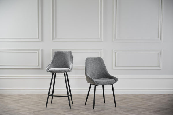 Grå stoppad matstol och barstol med svarta ben framför vit vägg med panel