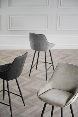 Moderna barstolar i grå och beige tyg med svarta ben mot vit vägg och ljust trägolv