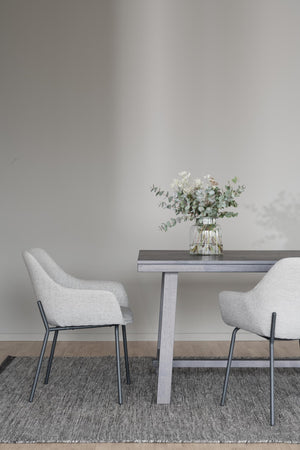 Matbord i grått trä med två vita stolar och vas med eukalyptus på grå matta