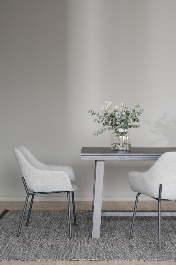 Matbord i grått trä med två vita stolar och vas med eukalyptus på grå matta