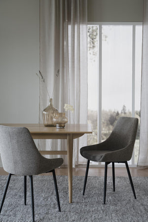 Grå matstolar med svarta ben runt matbord i ljus skandinavisk matsal med fönster och gardin