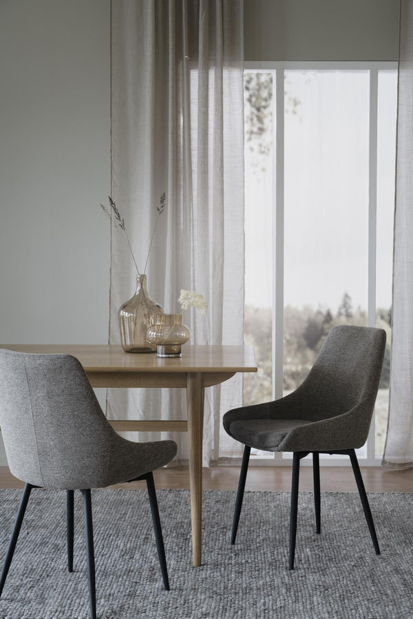 Grå matstolar med svarta ben runt matbord i ljus skandinavisk matsal med fönster och gardin