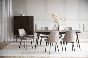 Matbord i mörkt trä med sex grå stolar i tyg, vit matta och beige väggdekor i skandinavisk matsal