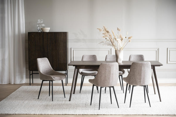 Matbord i mörkt trä med sex grå stolar i tyg, vit matta och beige väggdekor i skandinavisk matsal
