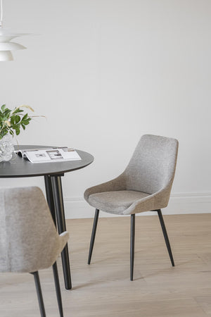 Grå stoppad matstol med svarta ben vid runt matbord i skandinavisk stil