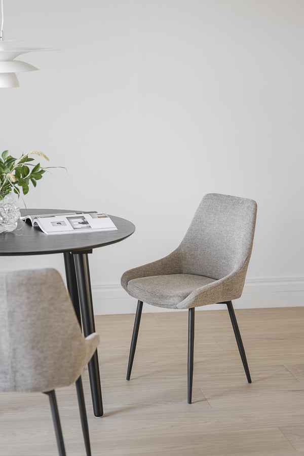 Grå stoppad matstol med svarta ben vid runt matbord i skandinavisk stil