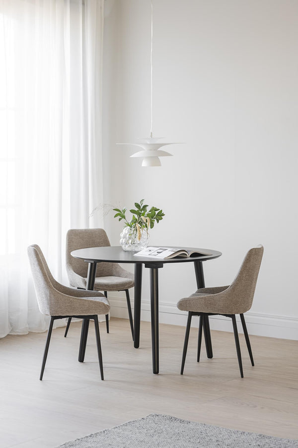 Rund matgrupp med svarta ben och fyra gråbeige stolar under modern taklampa i minimalistisk matsal