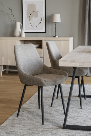 Grå matstol med svarta ben vid matbord i ljus modern matsal med sideboard och tavla