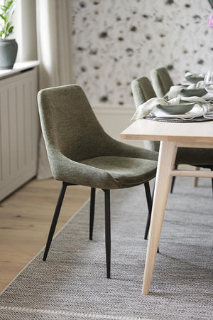 Gröna stoppade matstolar med svarta ben vid matbord i ljus modern matsal med floral tapet