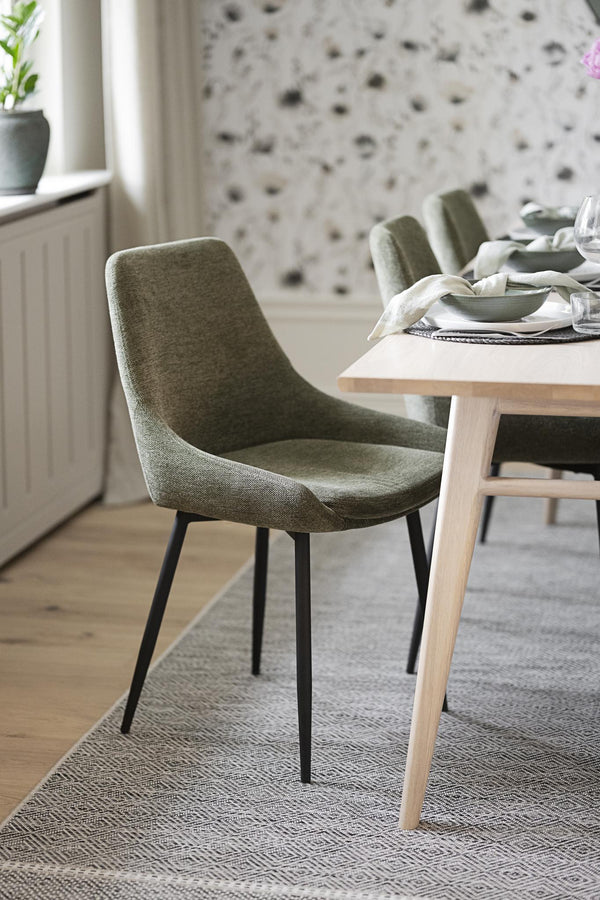 Gröna stoppade matstolar med svarta ben vid matbord i ljus modern matsal med floral tapet