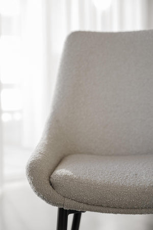 Närbild på grå stoppad stolsits med rundade kanter och svarta ben mot ljus bakgrund