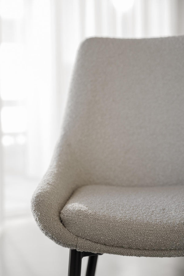 Närbild på grå stoppad stolsits med rundade kanter och svarta ben mot ljus bakgrund