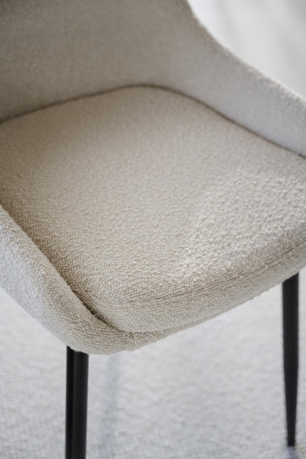 Närbild på beige fåtöljsits i bouclétyg med svarta ben, visar mjuk stoppning och textur