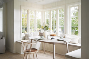 Ljust kök med sittbänk vid fönster, runt matbord och skandinavisk inredning i vitt och trä