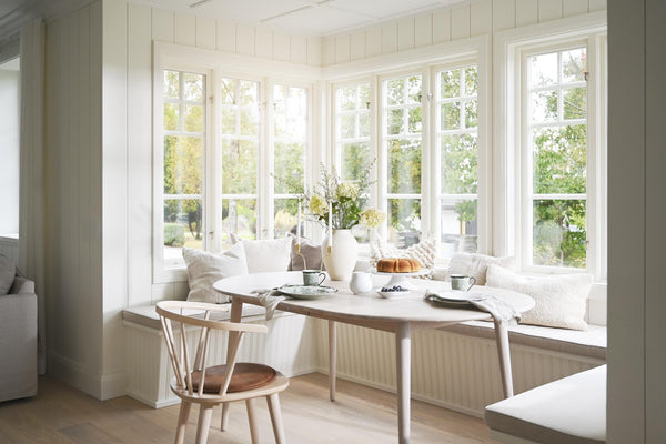 Ljust kök med sittbänk vid fönster, runt matbord och skandinavisk inredning i vitt och trä