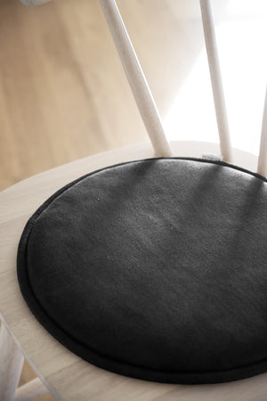Svart rund stolsdyna i läderimitation på vit trästol med spjälor