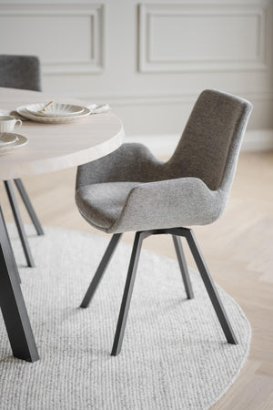 Grå matstol med armstöd och svarta ben vid vitt matbord i modern skandinavisk matsal