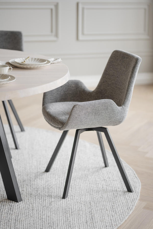 Grå matstol med armstöd och svarta ben vid vitt matbord i modern skandinavisk matsal