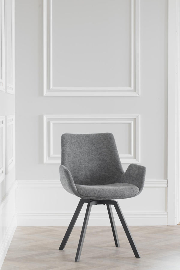 Grå matstol med armstöd och svarta ben i modern design mot vit vägg med tavelramar