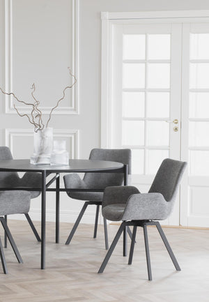 Grå matstol med armstöd och svarta ben vid runt matbord i modern matsal med ljusa väggar