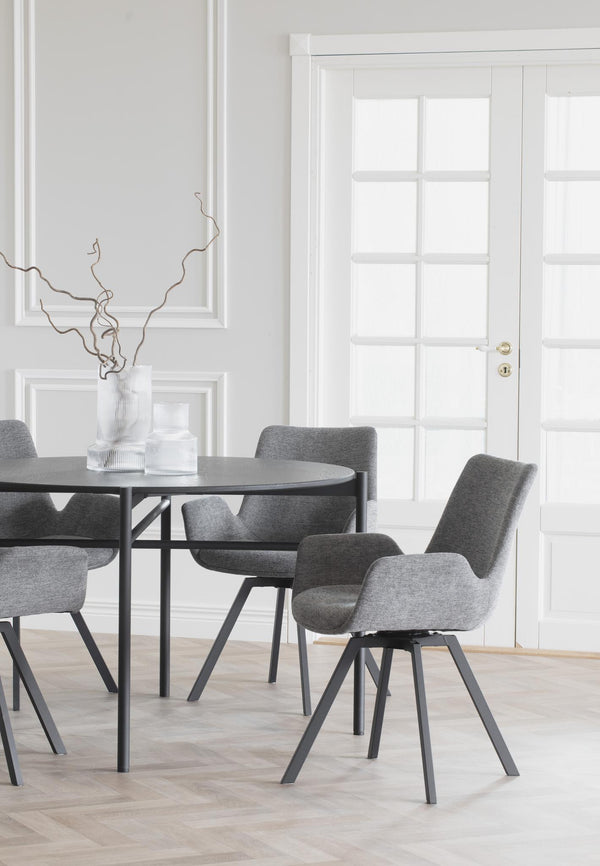 Grå matstol med armstöd och svarta ben vid runt matbord i modern matsal med ljusa väggar