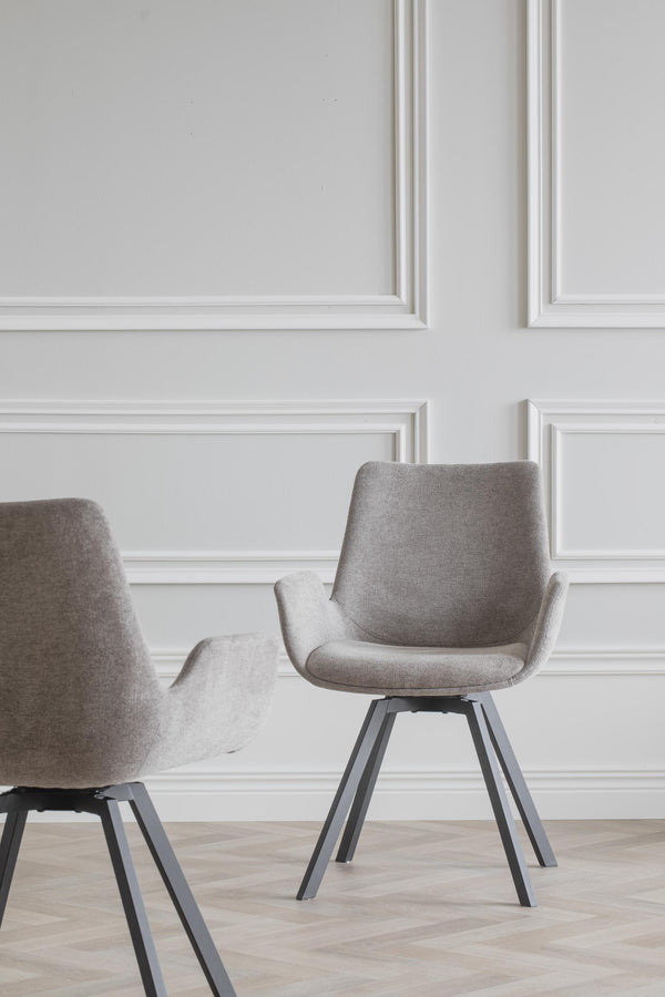 Grå matstolstolar med armstöd och svarta metallben framför vit vägg med taklist
