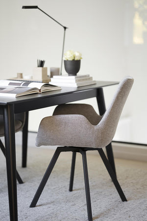 Grå stoppad stol med svarta ben vid svart skrivbord med lampa och böcker i modernt hemmakontor