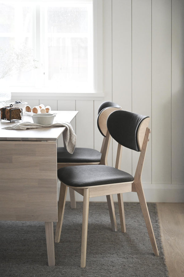 Matstol med stoppad sits och rygg i svart konstläder och stomme i ljust trä vid matbord i skandinavisk stil