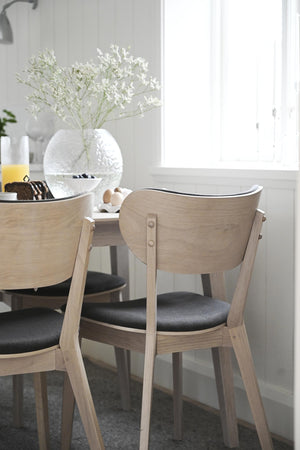 Ljusa trämatbordsstolar med svart sits vid runt matbord med vitfrostat glasvas och blommor