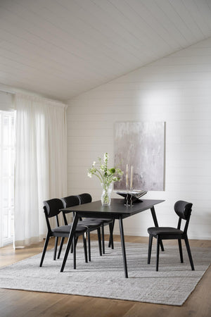 Svart matbord med matchande stolar i modern matsal med vita väggar och ljust trägolv