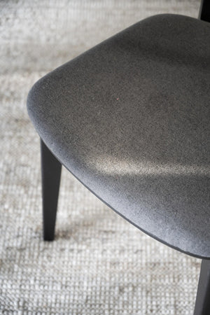 Närbild på grå stoppad stolsits med mjuk klädsel och svarta ben på ljus matta