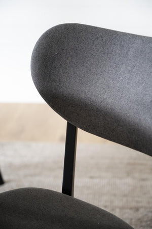 Närbild på ryggstöd på svart stol med mörkgrått tyg och svarta ben mot ljus bakgrund