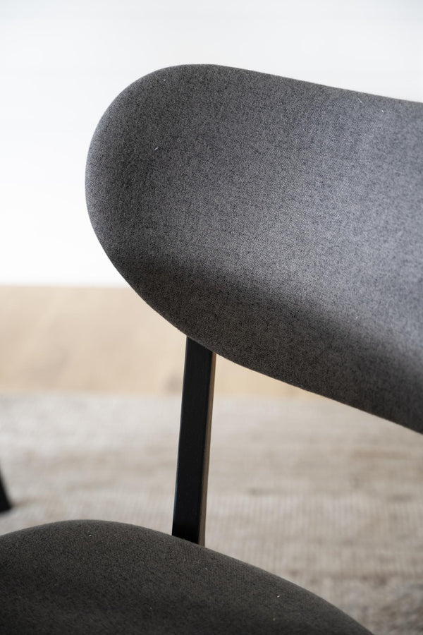 Närbild på ryggstöd på svart stol med mörkgrått tyg och svarta ben mot ljus bakgrund
