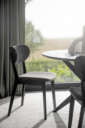 Svart stol med grå sits vid runt bord framför fönster med utsikt över naturlandskap