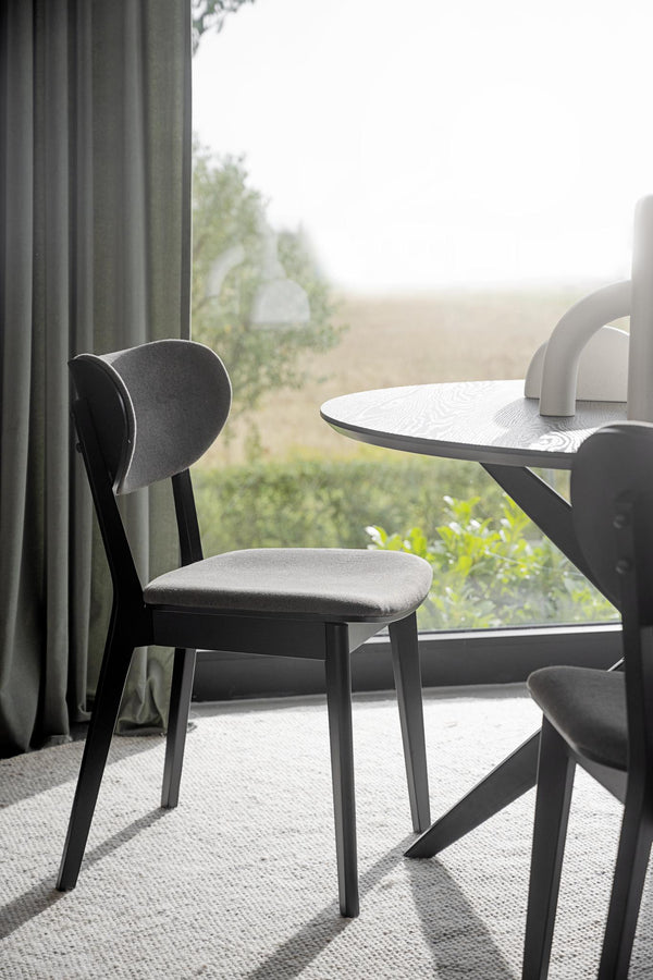 Svart stol med grå sits vid runt bord framför fönster med utsikt över naturlandskap