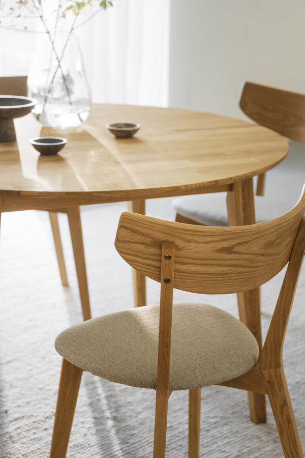 Matsalsstol i ljus ek med beige stoppning vid runt matbord i modern skandinavisk stil