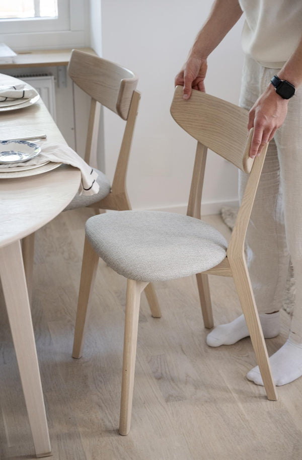 Ljus trässtol med stoppad sits och person som drar ut stolen från matbordet i skandinavisk matsal