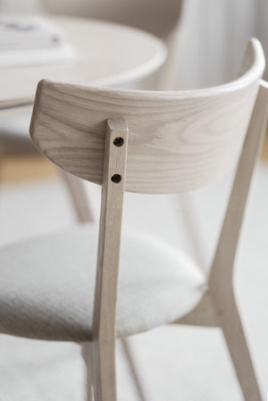 Närbild av stolsrygg i vitlaserad ek med synlig trästruktur och skruvinfästning mot vita mjuka textilier