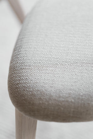 Närbild på ljusgrå stol med textilklädsel och träben, visar detaljer i tygets struktur och stolsits