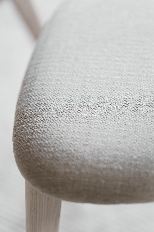 Närbild på ljusgrå stol med textilklädsel och träben, visar detaljer i tygets struktur och stolsits