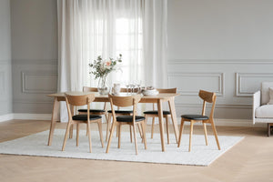 Matbord i ljust trä med sex stolar i skandinavisk design, dukat med porslin och blommor i ljust matrum