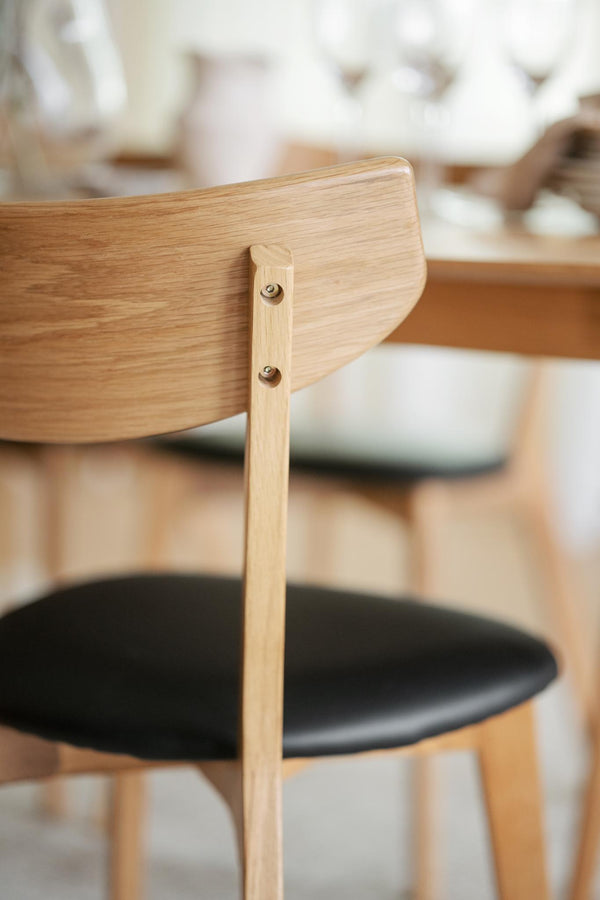 Närbild på ljus trässtol med svart sits och synliga skruvar i ryggstödet vid matbord