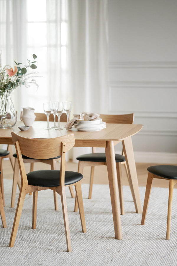 Matbord i ljust trä med matchande stolar med svarta dynor i modern skandinavisk matsal