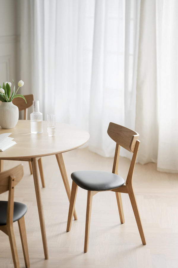 Ljus matsalsmiljö med rund träbord och stolar med grå sits och vita gardiner i bakgrunden