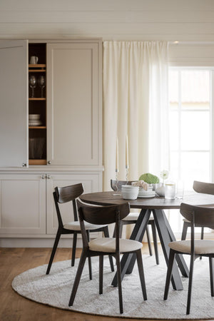 Matbord i mörkt trä med matchande stolar och ljusa dynor i skandinavisk matsal med vitrinskåp