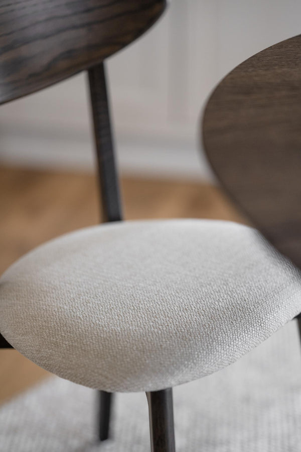 Matstol med ljusgrå tygsits och mörkt träben vid matbord med träskiva