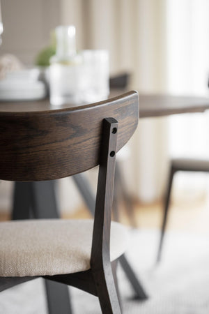 Närbild på ryggstöd i mörkbejsat trä med svart metallstöd på matstol med ljus dyna
