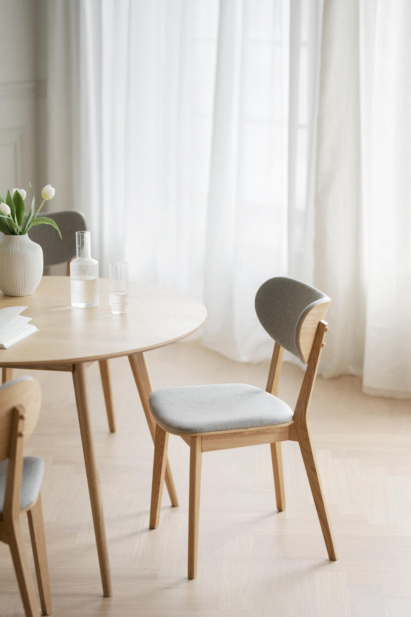 Matbord i ljust trä med stol i grå klädsel och vita tulpaner i vas, skandinavisk inredningsstil